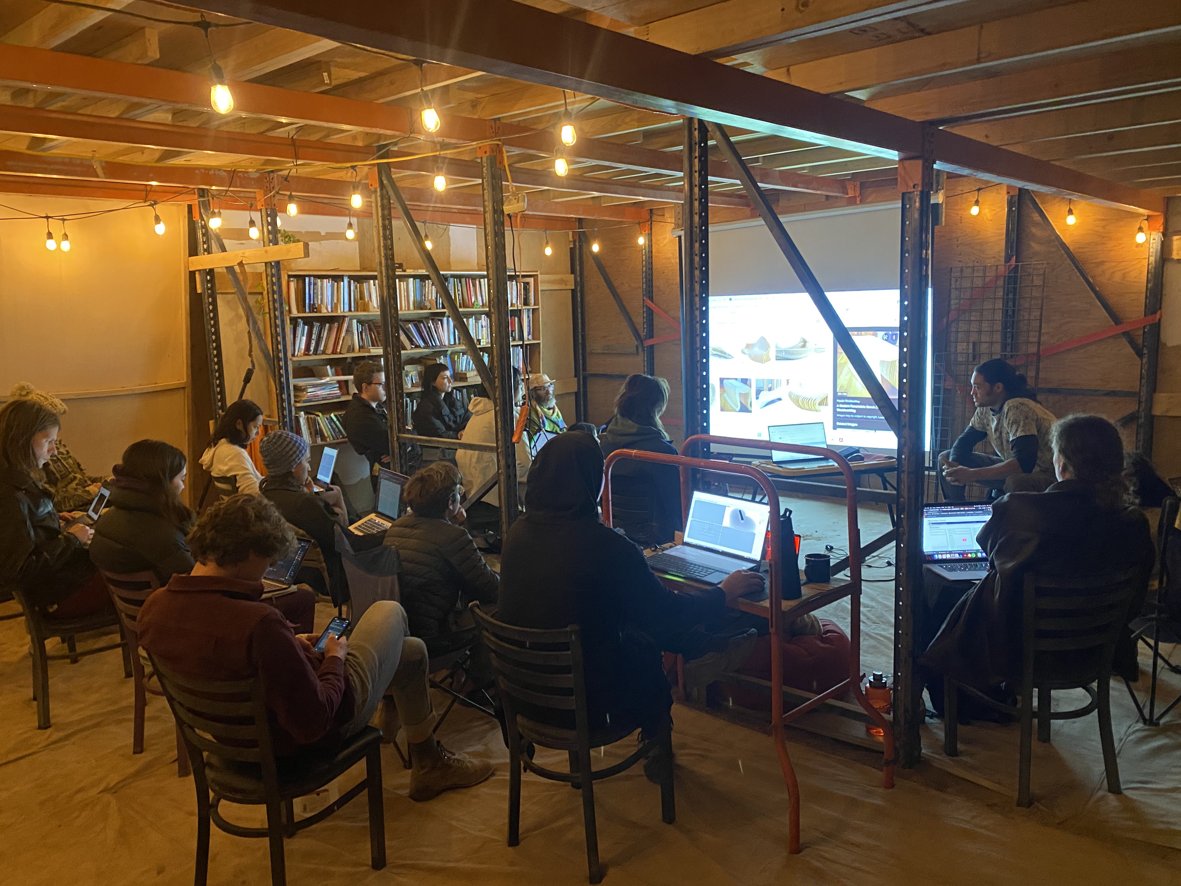A group of people in a workshop setting inside a room with pallet rack shelving.